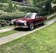 a red convertible car parked on the side of a road next to a lush green park