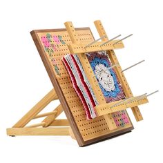 an easel with several knitting needles in it and a piece of cloth hanging from the pegs