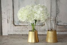 two vases with white flowers in them sitting on a table next to each other