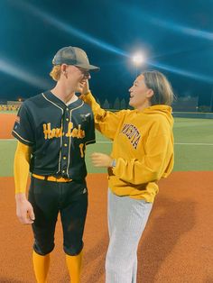 a man and woman in baseball uniforms standing on a baseball field at night with lights above them