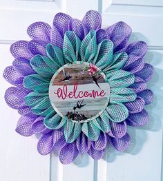 a purple and green mesh wreath with the words welcome on it hanging on a white door