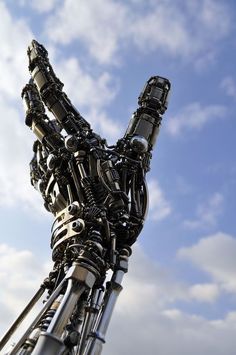 a large metal sculpture with many different parts on it's face and neck, against a blue sky with clouds