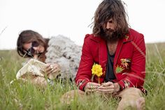 two people sitting in the grass and one is holding a flower