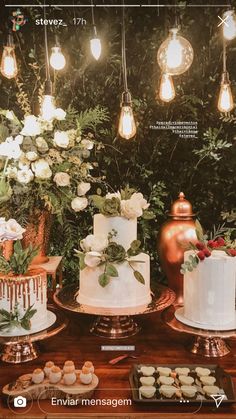 a table topped with lots of cakes and cupcakes next to lit bulbs hanging from the ceiling