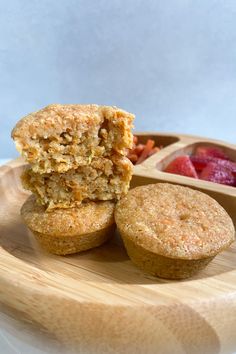 two muffins on a wooden plate with strawberries in the bowl and one half eaten