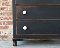 a black dresser with white knobs in front of a brick wall