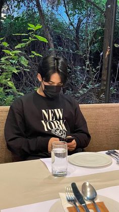 a woman sitting at a table wearing a black mask and looking at her cell phone