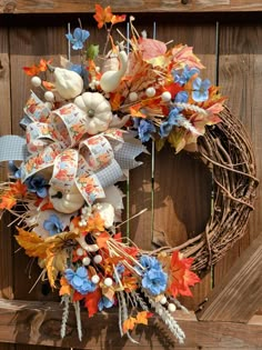 a wreath with pumpkins, leaves and other decorations on top of it in front of a wooden fence