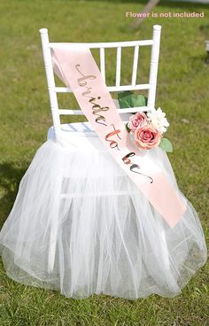 a white chair with a flower and sash on it sitting in the grass next to another chair