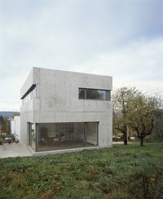 the house is made out of concrete and sits on top of a grassy hill with trees in the background