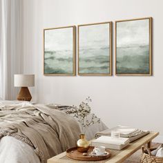 a bedroom with three paintings on the wall and a coffee table in front of it