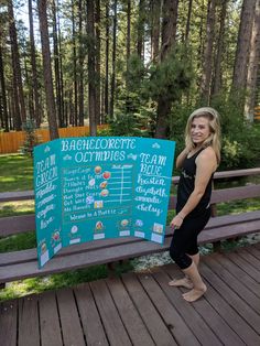 a woman standing next to a sign on a wooden deck in front of some trees