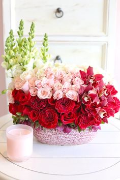 a vase filled with red and white flowers on top of a table next to a candle