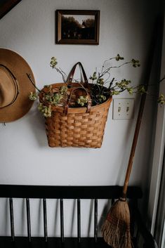 a basket with flowers and a broom hanging on the wall next to a hat rack