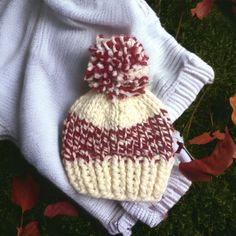 a white and red knitted hat laying on top of a blanket in the grass