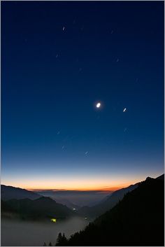 the sun is setting over mountains with fog in the foreground and stars in the sky