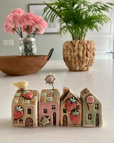 small ceramic houses with strawberries painted on them sitting on a table next to a potted plant