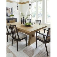 a dining room table with chairs and a bowl of fruit on the table in front of large windows