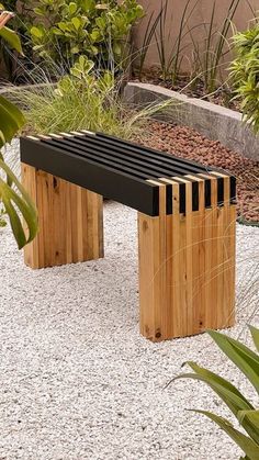 a wooden bench sitting on top of a gravel covered ground next to trees and bushes