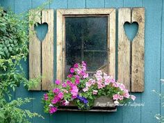 a window box filled with flowers next to a blue wall and wooden shutters on the side of a building