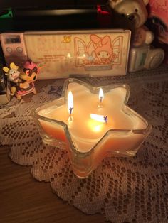 two lit candles sitting on top of a doily next to a small teddy bear