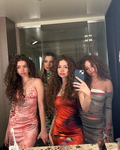 three women taking a selfie in front of a mirror with one woman holding a cell phone