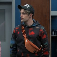 a man in a black hat and tie dye sweatshirt with a fanny bag on his shoulder