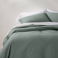 an unmade bed with green sheets and pillows