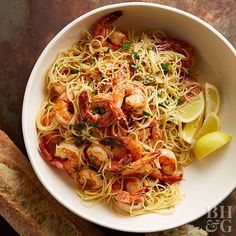 a white bowl filled with pasta and shrimp on top of a table next to bread