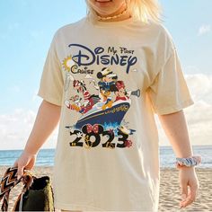 a woman standing on top of a sandy beach next to the ocean wearing a mickey mouse t - shirt