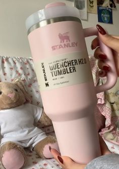 a person holding a pink coffee cup next to a teddy bear on a bed with sheets