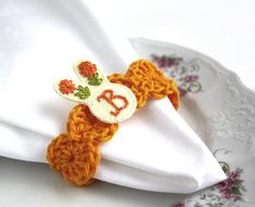 a white plate topped with an orange and yellow crochet bunny napkin ring on top of a white cloth