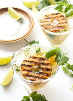 two glasses filled with drinks and garnished with limes