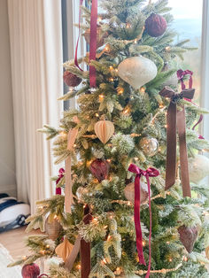 a decorated christmas tree with red ribbon and ornaments on it in front of a window