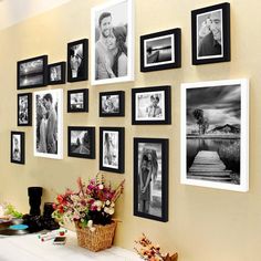 a bunch of pictures hanging on the wall above a table with flowers and vases