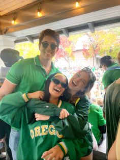 two people in green shirts and sunglasses hugging each other at a sporting event with an audience behind them