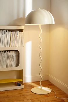 a floor lamp sitting next to a book shelf filled with books and cds on top of a hard wood floor