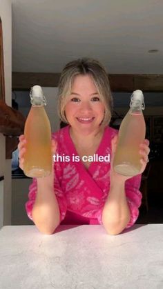 a woman sitting at a table with two bottles of liquid in front of her and the caption, this is called