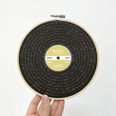 a hand is holding up a record that has been embroidered onto it with words on the side