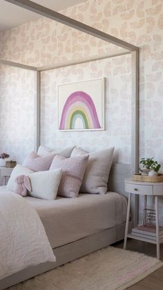 a white bed with pink pillows and a rainbow painting on the wall behind it in a bedroom