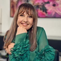 a woman with long hair wearing a green top and smiling at the camera, in front of paintings