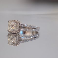 an engagement ring with two matching bands and a cushion cut diamond in the center, on a reflective surface