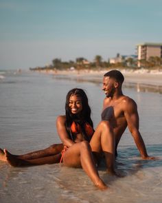 a man and woman are sitting in the water at the beach, posing for a photo