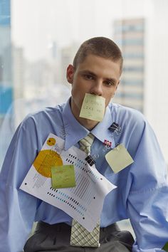 a man sitting in front of a window with papers taped to his mouth and sticky notes attached to his nose