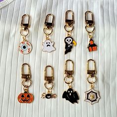 six halloween themed keychains on a white fabric background, one has a ghost, the other is a jack - o'- lantern