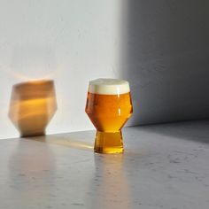 a glass of beer sitting on top of a counter next to a wooden vase with a light coming from it