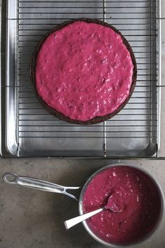 a cake on a cooling rack with a pink frosting in the middle and a bowl next to it