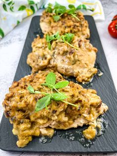 three pieces of chicken covered in sauce and garnished with fresh herbs on a black plate