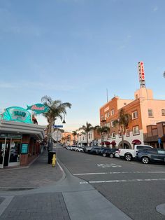 cars are parked on the street in front of some buildings and palm trees at sunset