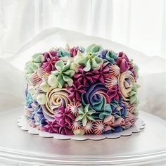 a multicolored cake with flowers on it sitting on top of a white table